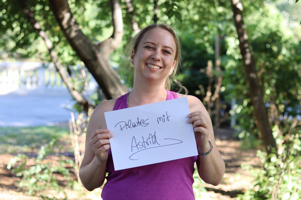 Trainerin Astrid Entlesberger, mit Schild "Pilates mit Astrid"